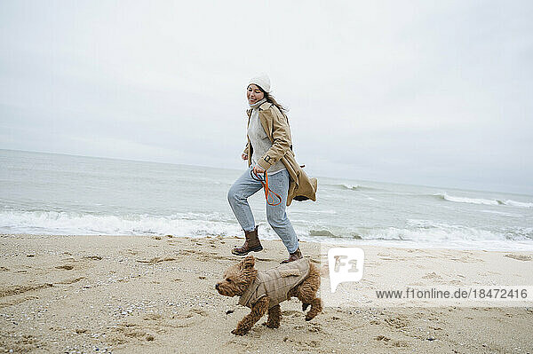Frau läuft mit Hund in Ufernähe am Strand
