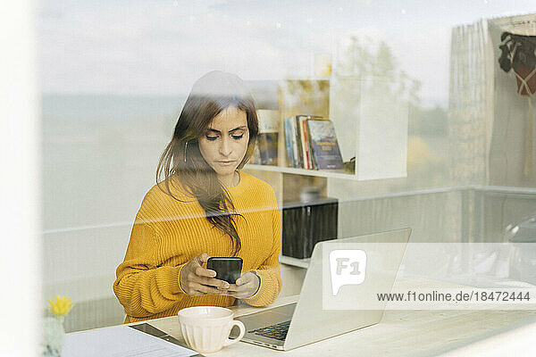 Businesswoman using smart phone seen through glass