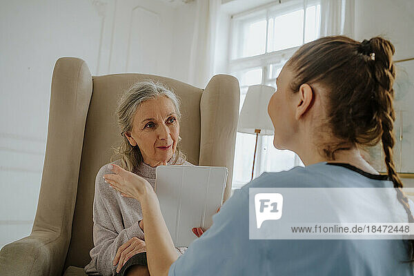 Senior woman looking at caregiver holding tablet PC at home