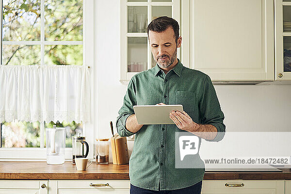 Mature man using digital tablet standing in the kitchen