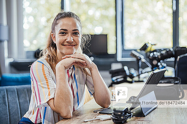 Smiling businesswoman with hand on chin sitting at desk