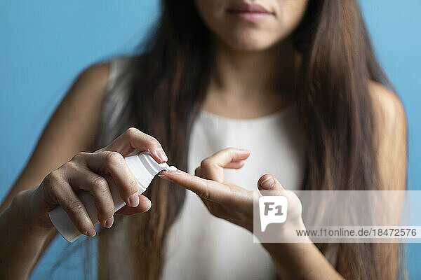 Woman applying cream on finger against blue background