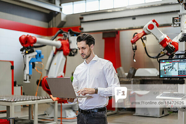 Engineer using laptop standing in robot factory