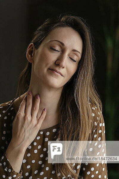 Smiling woman with eyes closed touching neck