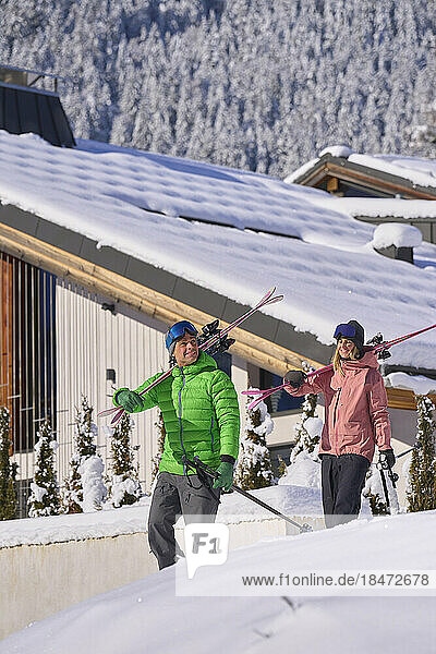 Man and woman carrying skis walking in front of chalet