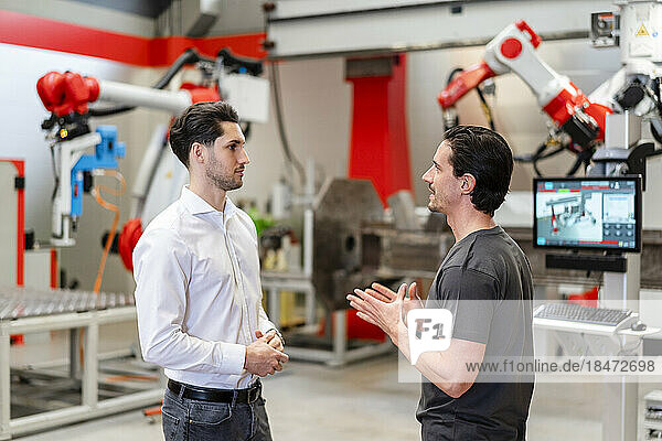 Engineer discussing with colleague standing in robot factory