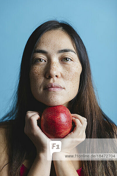 Woman holding pomegranate fruit against blue background