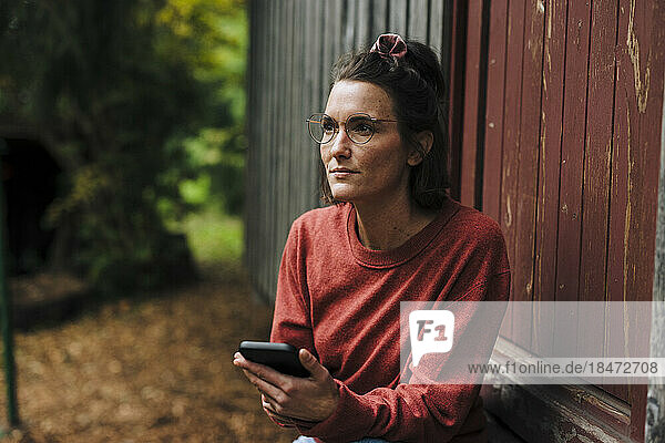 Thoughtful woman with mobile phone sitting in doorway
