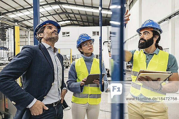 Engineer with note pad explaining colleagues in factory