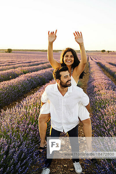 Happy woman enjoying piggyback ride on man in lavender field