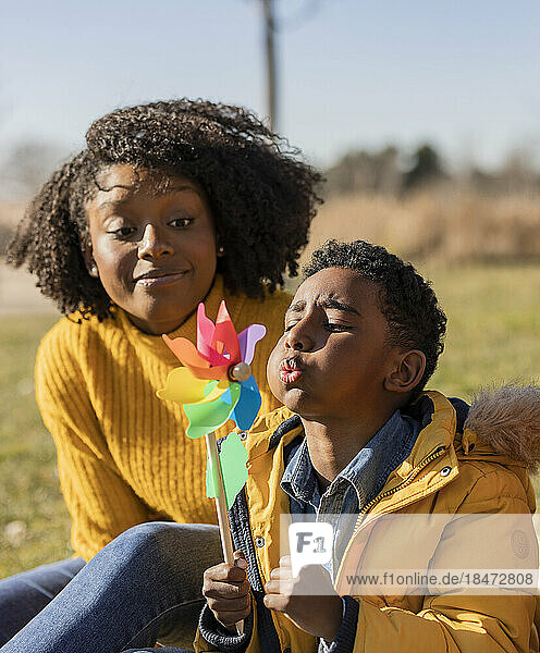 Boy blowing pinwheel with mother in park on sunny day