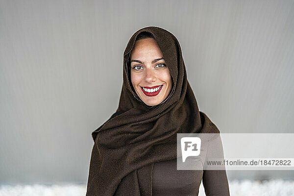 Happy woman wearing hijab in front of gray wall