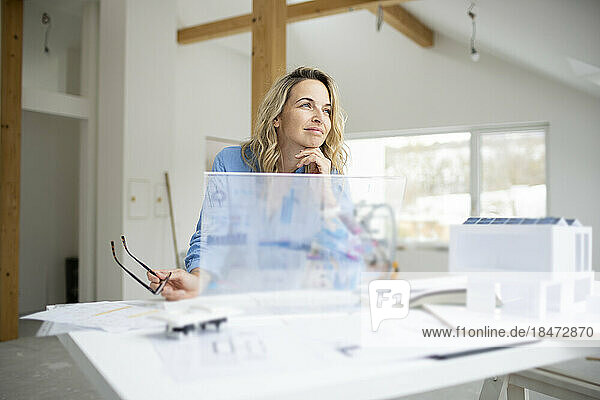 Nachdenklicher Architekt mit Hand am Kinn und transparentem Tablet-PC am Schreibtisch
