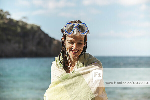 Smiling woman wrapped in blanket wearing diving goggles