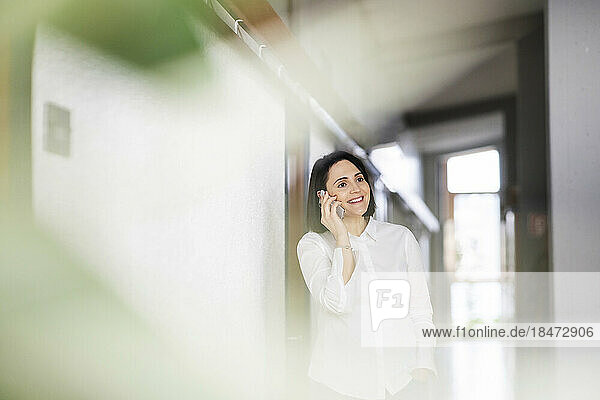 Smiling woman talking on mobile phone standing by wall