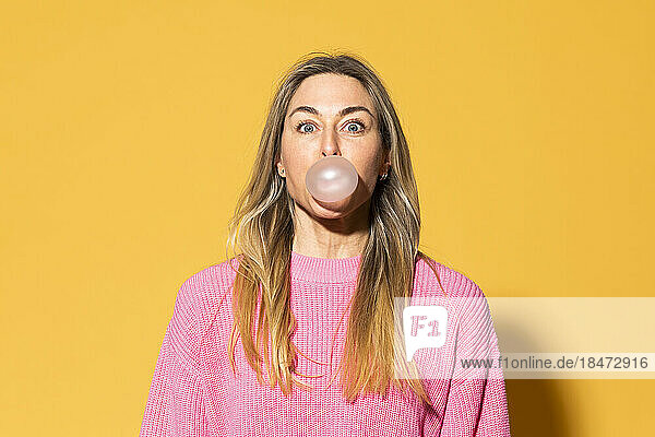 Woman blowing bubble gum against yellow background