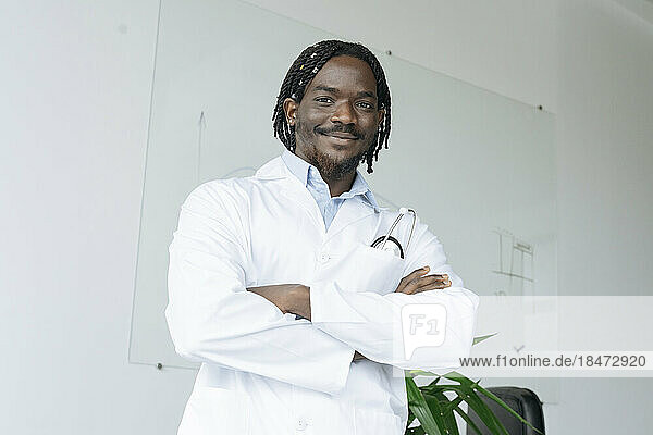 Smiling doctor standing with arms crossed at clinic