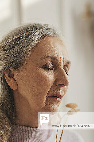 Senior woman with eyes closed and dry plant at home