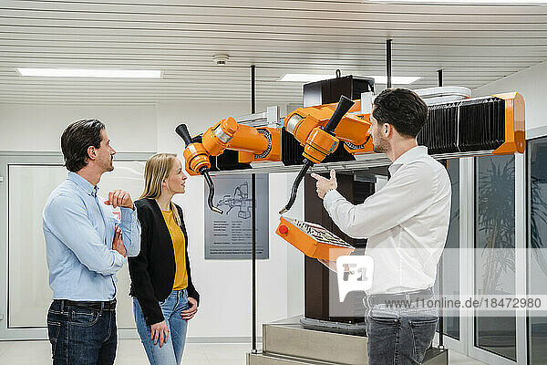 Technician operating robots near colleagues in factory
