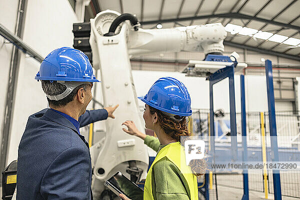 Engineers wearing hardhat having discussion in front of robotic arm at factory