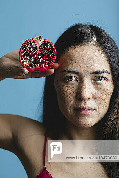 Woman with freckles on face holding pomegranate fruit