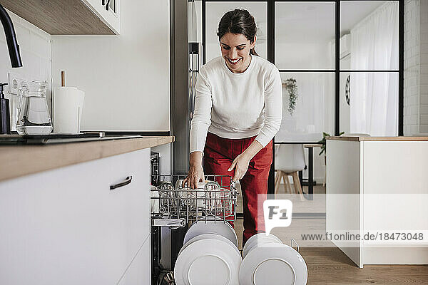 Lächelnde Frau ordnet zu Hause Tassen in der Spülmaschine