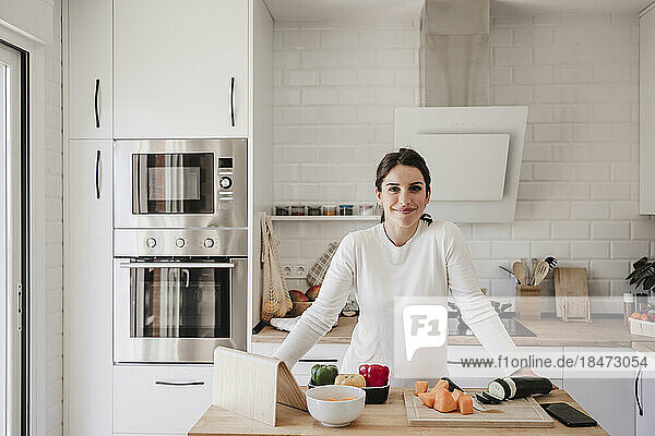 Smiling woman standing with vegetable on table in kitchen at home