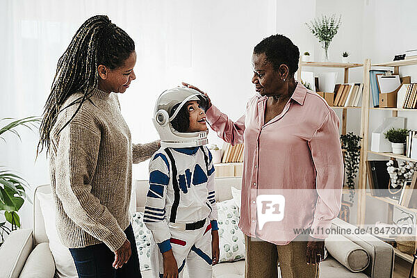 Mother and grandmother looking at granddaughter wearing space suit at home
