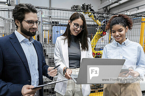 Happy businesswoman sharing laptop with colleague in factory