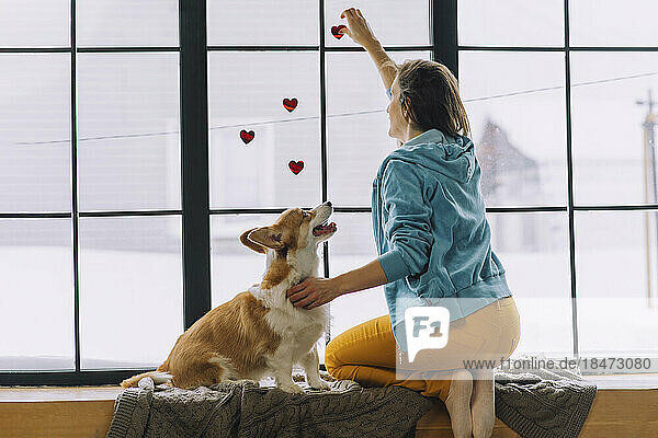 Frau klebt zu Hause neben Hund Herzaufkleber ans Fenster
