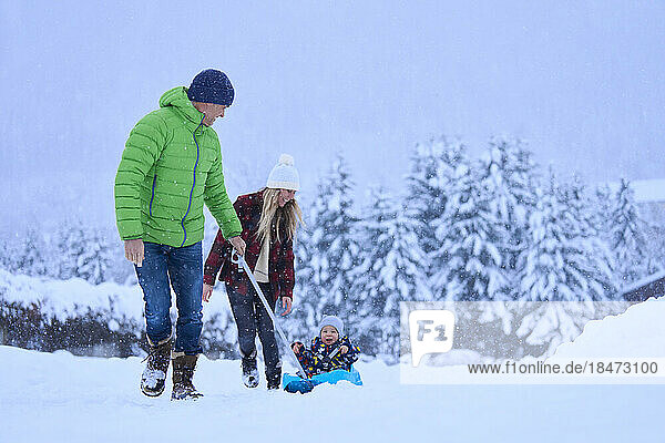 Mother and father with son sitting on sled in snow