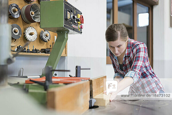 Craftswoman cutting wood with machine in workshop