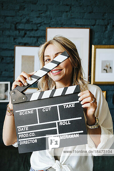 Smiling actress holding clapboard on film set