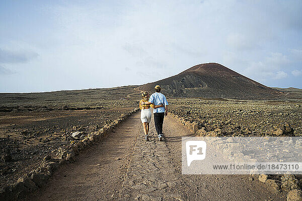 Junges Paar läuft auf unbefestigter Straße in vulkanischer Landschaft