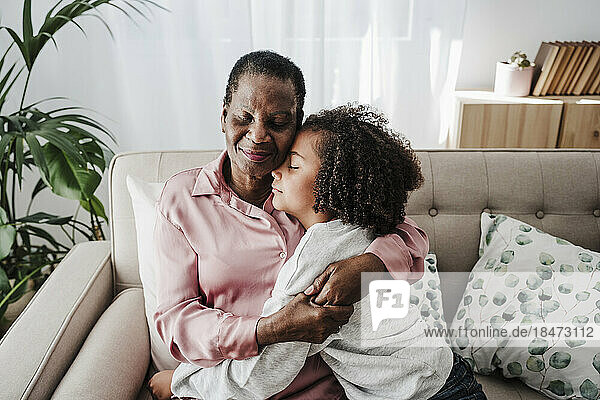 Girl resting with grandmother sitting on sofa at home