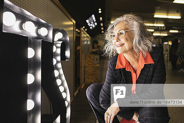 Happy businesswoman in squatting position looking at illuminated sign