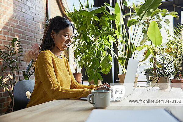 Smiling businesswoman surfing net through laptop at loft office