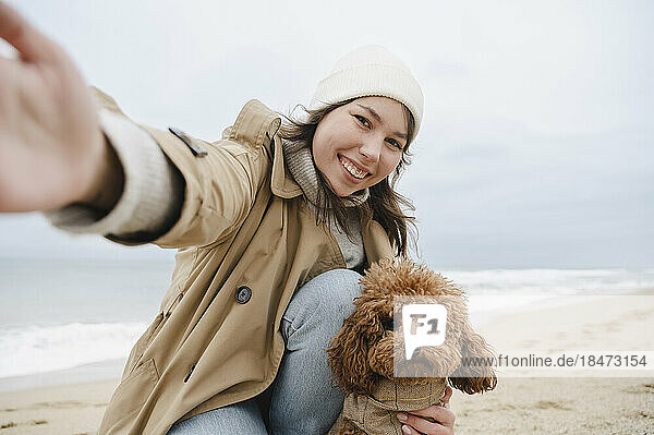 Glückliche Frau macht Selfie mit Hund am Strand