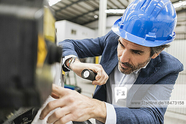 Engineer holding torch analyzing machine part in factory