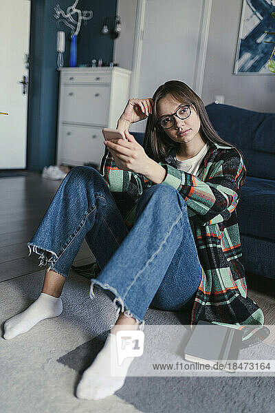 Young woman wearing eyeglasses sitting with mobile phone at home
