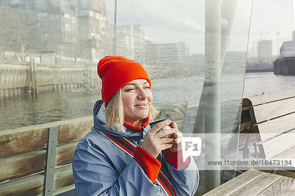 Woman drinking coffee sitting on bench at ferry terminal