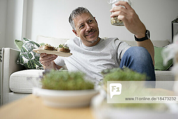 Happy man holding sprouts jar in living room at home