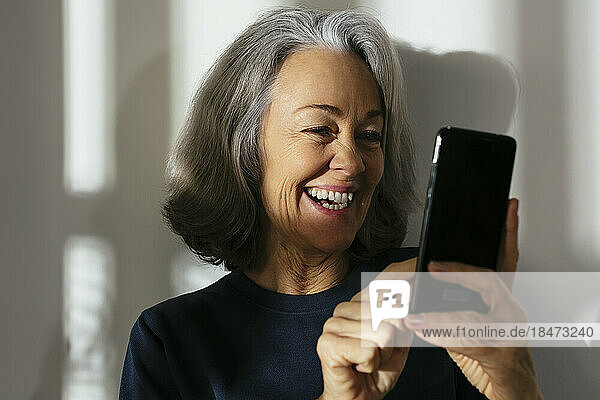 Smiling mature woman using smart phone in front of wall