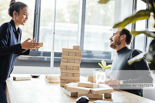 Smiling businesswoman with colleague stacking up wooden blocks in office