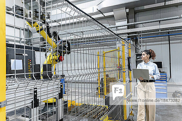 Young businesswoman standing with laptop in factory