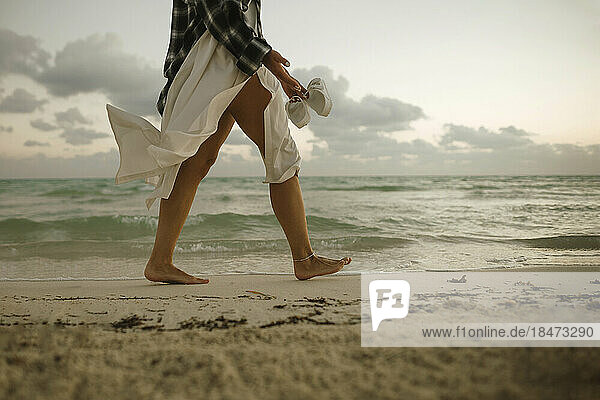 Woman walking barefoot on sand near shore at beach
