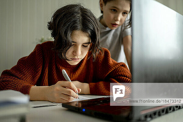 Boy doing homework with brother in background at home
