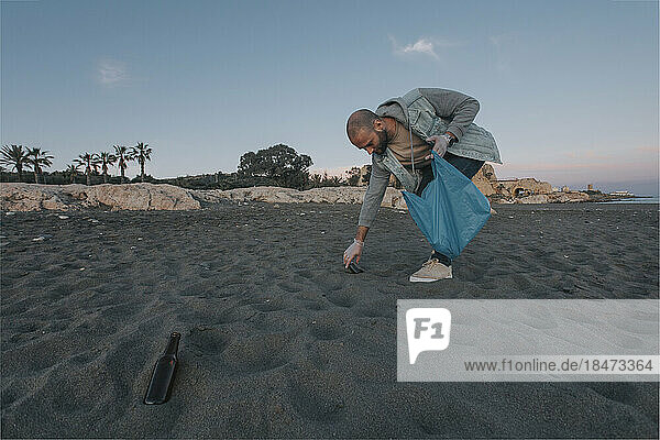 Mann sammelt Müll in Plastiktüte vom Strand