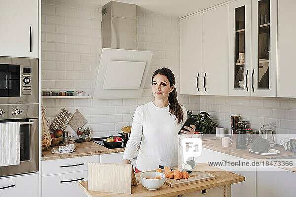 Nachdenkliche Frau steht mit Smartphone in der Küche