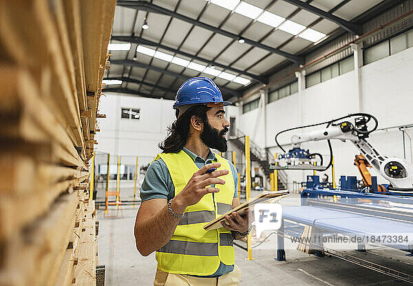Engineer with note pad standing by stack of planks in factory